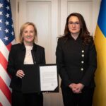 Представниці України та США з документом на тлі прапорів держав