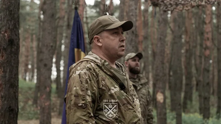 Командир 155-ї бригади у камуфляжі на тлі прапора України в лісі