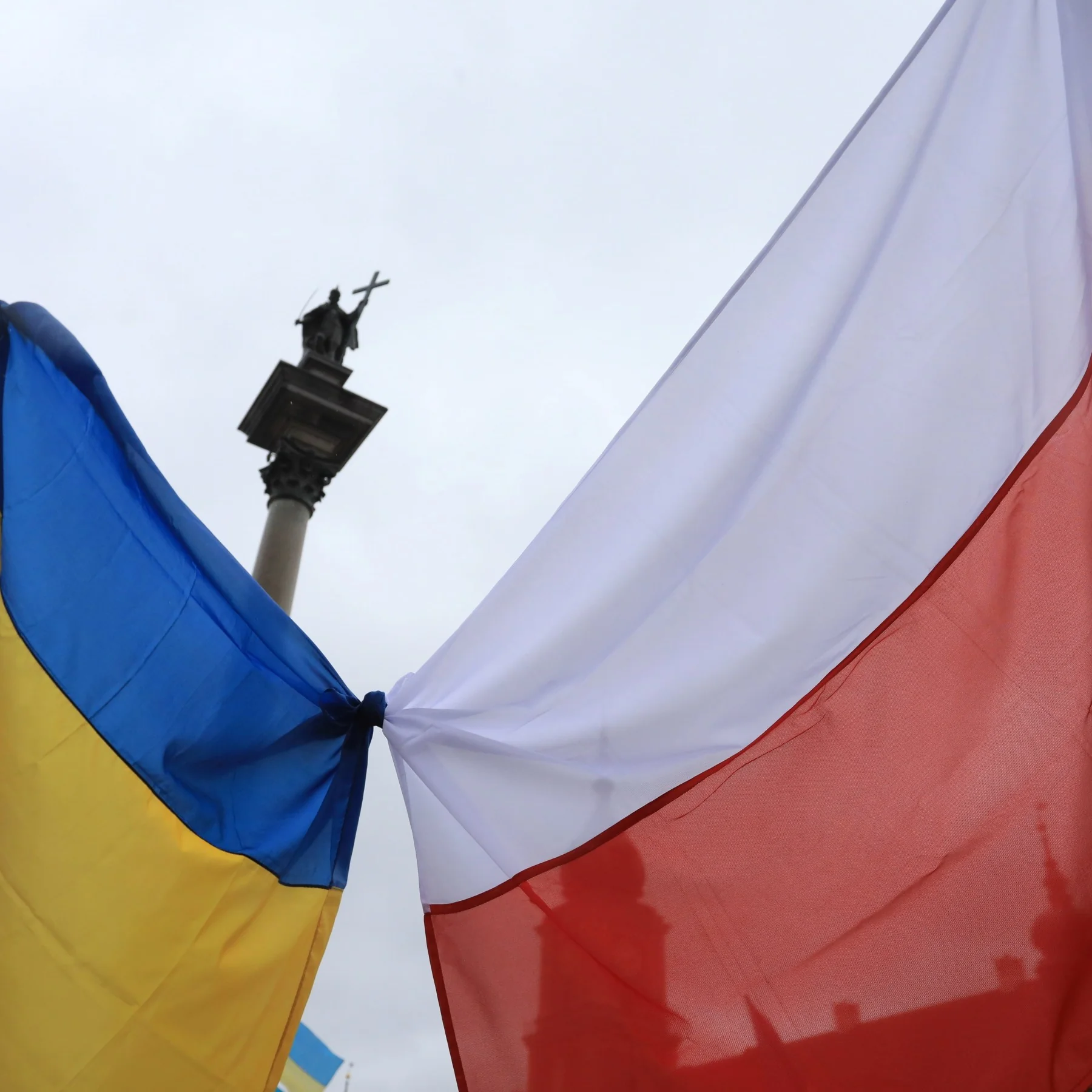 Прапори України та Польщі, завязані разом, на тлі колони Сигізмунда у Варшаві