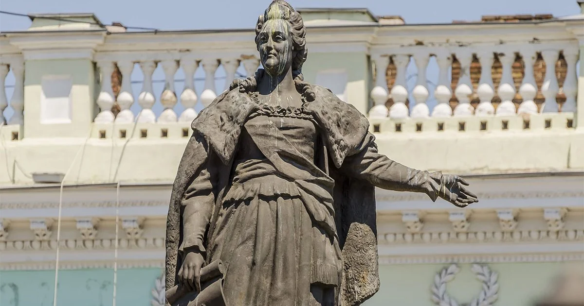 Бронзовий памятник Катерині ІІ зі сувоєм і простягнутою рукою на тлі будівлі