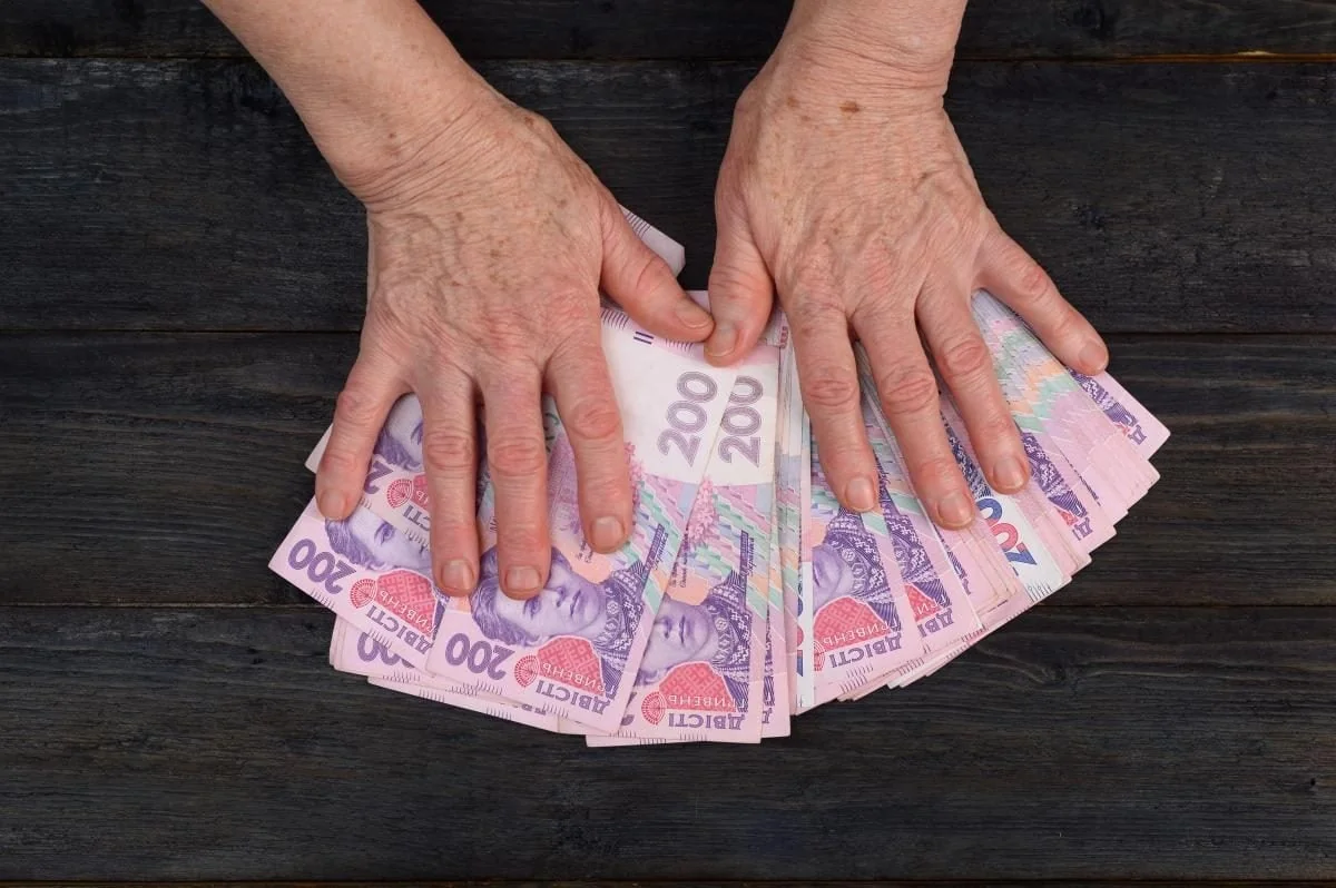Пожилые руки держат банкноты по 200 гривен для пенсии