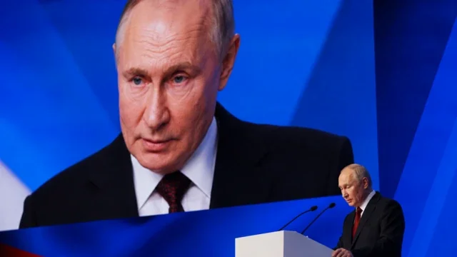 Путін за трибуною на тлі великого портрета свого обличчя