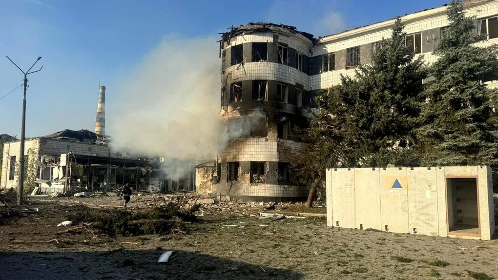 Зруйнована біла будівля з димом, уламками та людиною серед руїн