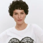 Даша Астаф’єва з короткою кучерявою зачіскою в білій футболці з мереживним принтом